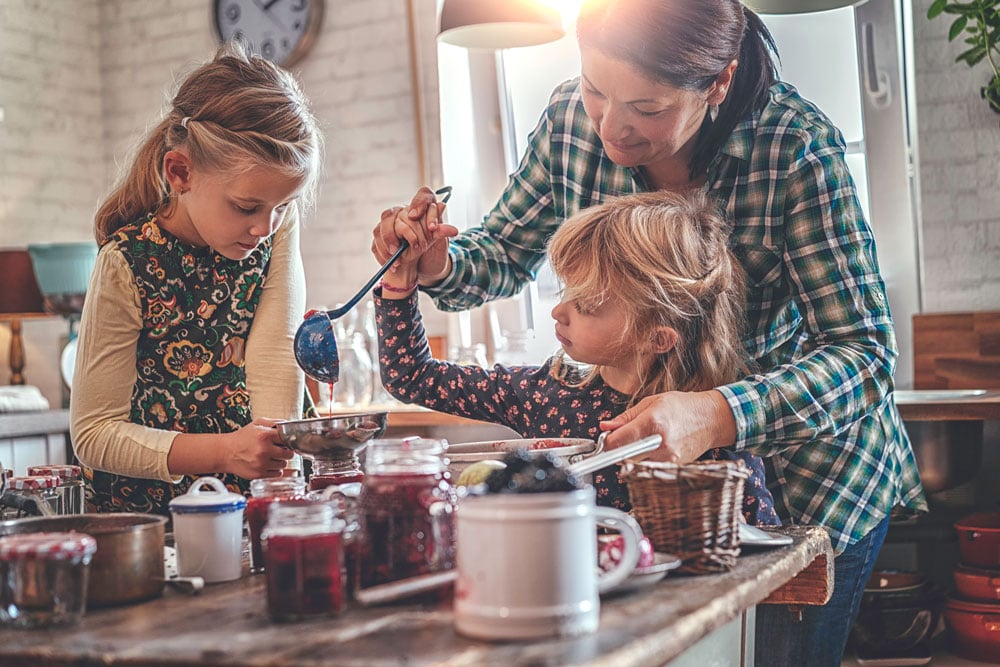 Mother and two daughters making fruit preserves in kitchen