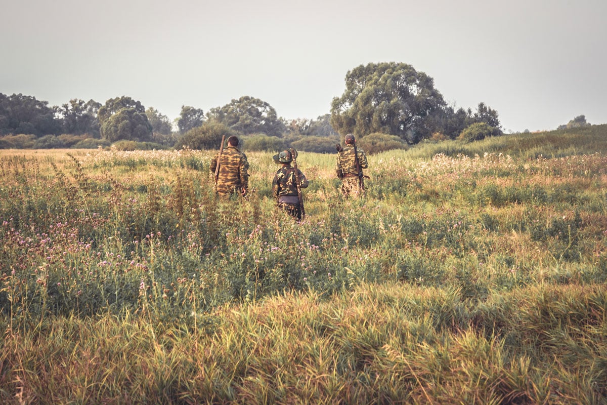 three men in camo in an open field 